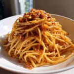 A close-up, appetizing shot of a mound of glossy garlic noodles topped with crispy fried garlic pieces.