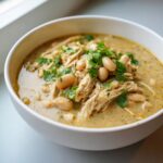 Close-up of a white bowl filled with creamy instant pot white chicken chili, featuring shredded chicken, white beans, and fresh cilantro.