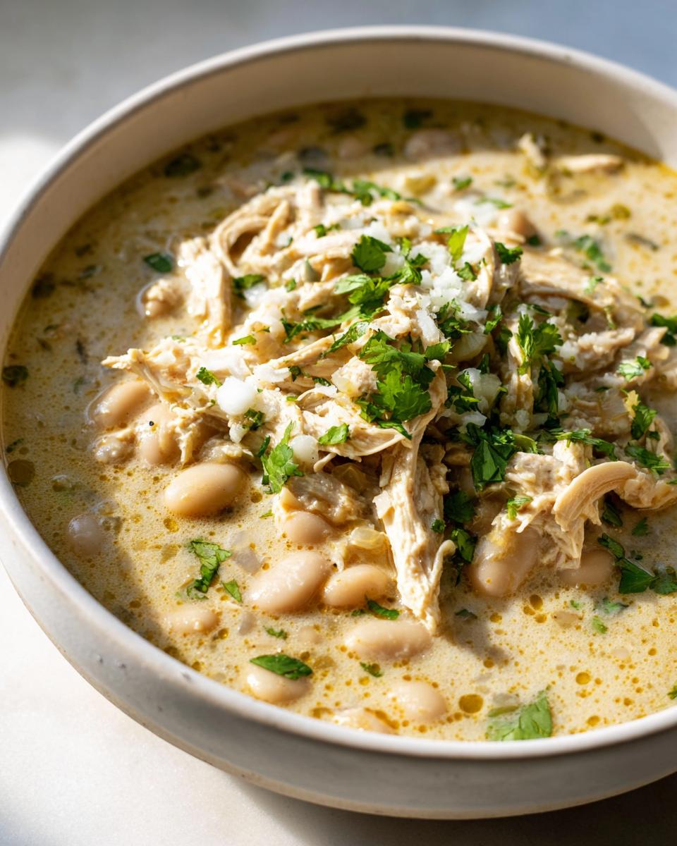 Close-up of a creamy bowl of instant pot white chicken chili topped with shredded chicken, white beans, and fresh cilantro.
