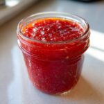 Close-up of a glass jar filled with vibrant red strawberry freezer jam, showing visible seeds and texture.