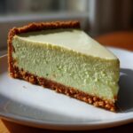 A single, thick slice of creamy key lime cheesecake with a golden graham cracker crust, sitting on a white plate.