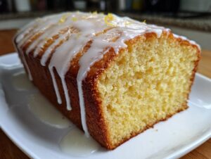 Close-up of a freshly baked lemon pound cake loaf, drizzled with white glaze and lemon zest.