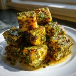 A stack of cubed marinated cheese generously coated in green herbs and oil, ready to serve.