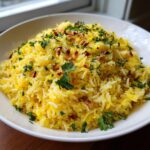 A white bowl filled with vibrant yellow mediterranean rice, topped with toasted pine nuts and fresh chopped parsley.