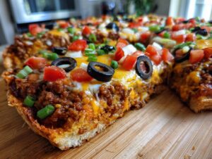 Close-up view of a thick slice of Mexican pizza loaded with seasoned ground beef, melted cheese, black olives, tomatoes, and green onions.