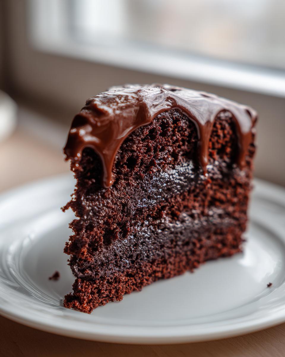 Close-up of a rich, moist slice of chocolate cake recipe topped with dripping chocolate ganache.