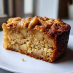 Close-up of a moist slice of jewish apple cake showing tender crumb and visible apple chunks.
