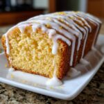 A close-up of a moist lemon pound cake drizzled with white icing and topped with zest.