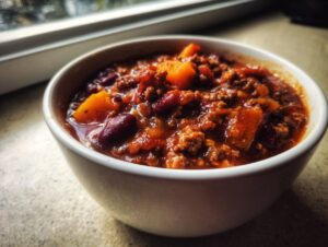 Close-up of a white bowl filled with rich, chunky pumpkin chili featuring ground meat, kidney beans, and squash chunks.