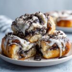 Three stacked, gooey Oreo cinnamon rolls covered in white icing and crushed cookie pieces.