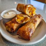 Close-up of crispy, golden brown peach cobbler egg rolls, one cut open showing the sweet peach filling.