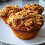 Close-up of three golden-brown pecan pie muffins topped with a generous, crunchy pecan streusel topping.