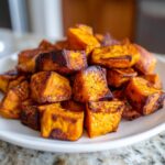 A close-up pile of perfectly roasted sweet potato cubes with caramelized edges served on a white plate.
