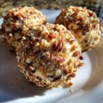 Close-up of three delicious pineapple cheese ball appetizers coated in chopped pecans and spices on a white plate.