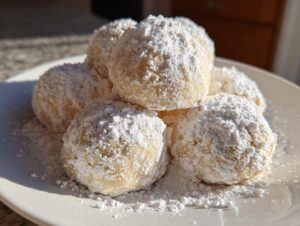A close-up stack of freshly baked russian tea cakes heavily dusted with powdered sugar on a white plate.