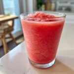 A tall glass filled with a bright red, icy watermelon smoothie, ready to drink.