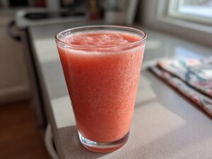 A tall glass filled with a vibrant, icy watermelon smoothie sitting on a sunlit countertop.