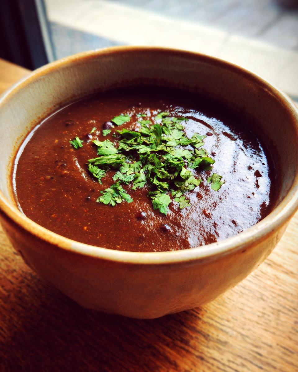 Close-up of a thick, dark brown black bean soup topped with fresh chopped cilantro in a rustic bowl.