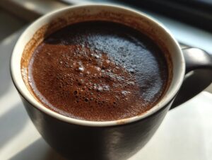 Close-up of rich, dark french hot chocolate with a layer of fine foam in a dark mug.