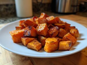 A close-up of perfectly caramelized roasted sweet potatoes cubes served on a white plate.