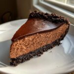 A perfect slice of rich chocolate cheesecake with a dark chocolate ganache topping and crumb crust.