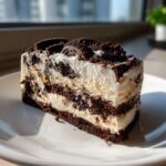 A rich slice of layered dirt cake featuring cream filling and dark chocolate cookie crumbs, topped with whole mini Oreos.