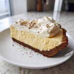 A thick slice of creamy eggnog pie with a dark crust, topped with whipped cream and nutmeg.