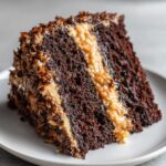 Close-up of a moist slice of german chocolate cake recipe with thick coconut-pecan frosting.