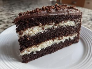 A tall slice of decadent german chocolate cake recipe showing three dark chocolate layers separated by thick coconut-pecan filling.