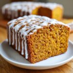 Close-up of a slice of moist pumpkin bread topped with a thick white vanilla glaze.