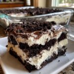 A close-up slice of Oreo dirt cake showing layers of dark chocolate cookie crumbs and white creamy filling.