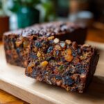 Close-up of a thick slice of dark, moist fruit cake recipe packed with raisins and candied peel.