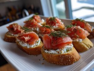 Close-up of several smoked salmon bites served on toasted bread with cream cheese and dill.