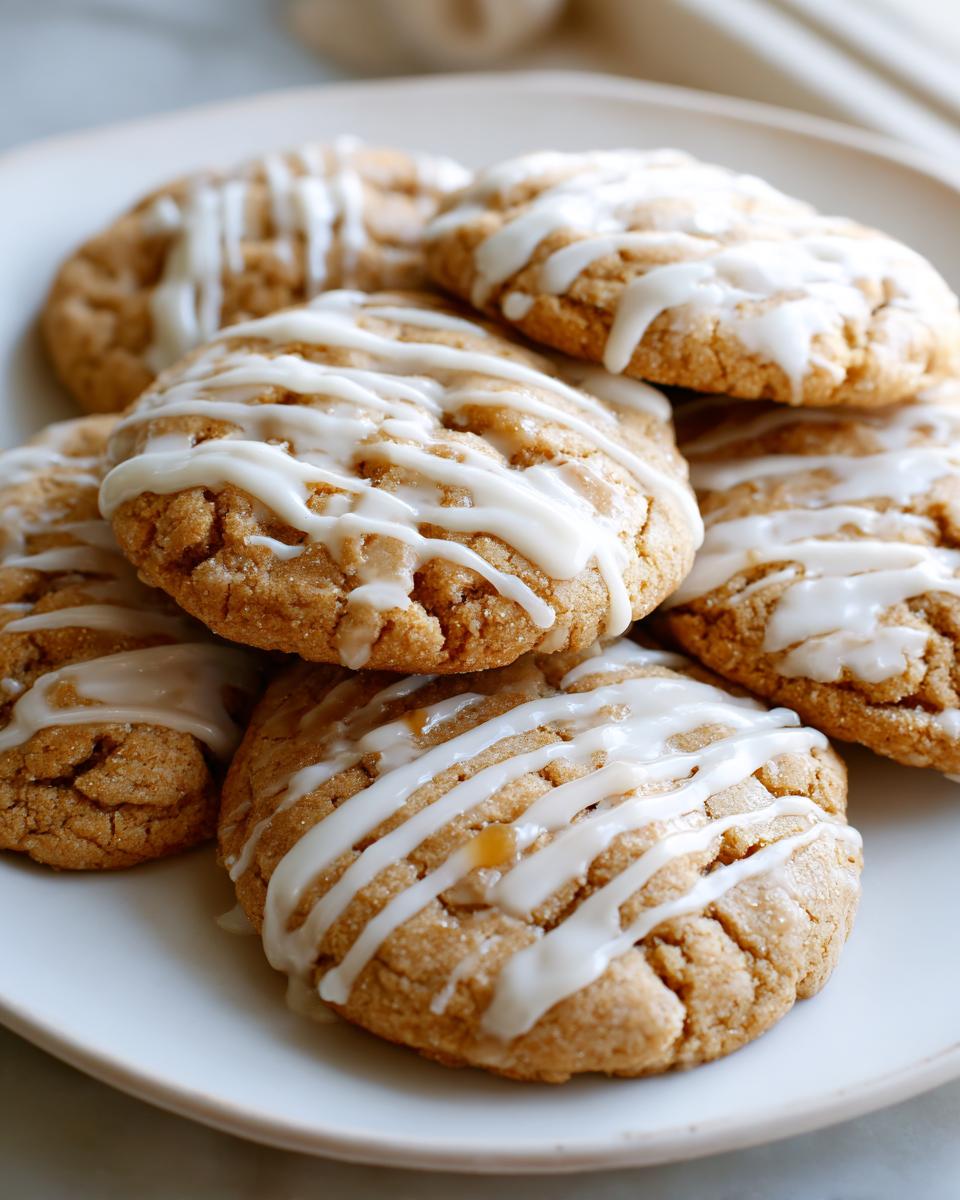 A stack of soft maple brown sugar cookies drizzled generously with white vanilla glaze on a light plate.