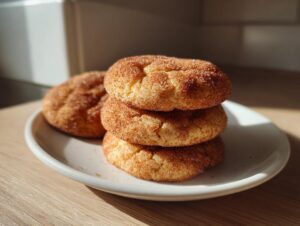 A stack of three soft snickerdoodle cookies generously coated in cinnamon sugar resting on a small white plate.