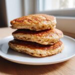 A close-up stack of three golden brown banana oatmeal pancakes on a white plate.