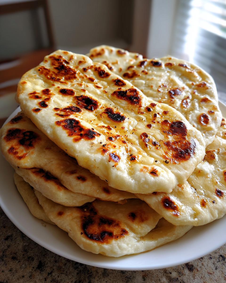 A stack of freshly made naan bread with characteristic charred bubbles piled on a white plate.