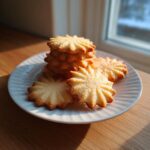 A stack of golden brown, star-shaped butter cookies resting on a white plate near a window.