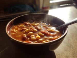 A steaming bowl of rich, tomato-based pasta fagioli featuring ditalini pasta and beans, ready to eat.
