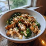 Close-up of a sticky chicken rice bowl featuring glazed chicken pieces, bright green broccoli, and a drizzle of creamy sauce.