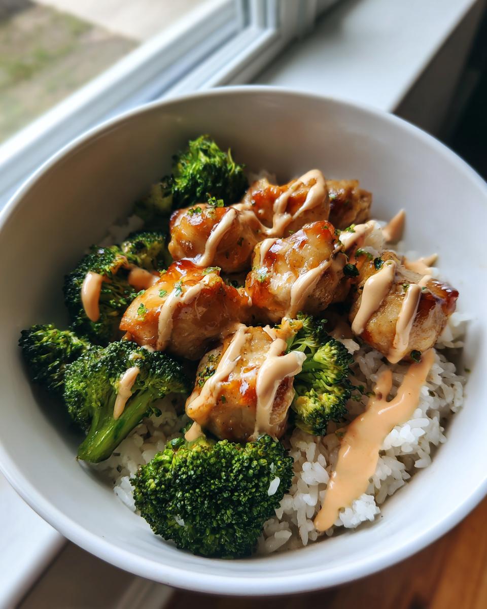 A close-up of a vibrant chicken rice bowl featuring sticky glazed chicken pieces, bright green broccoli florets, and a drizzle of sauce.
