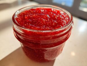 Close-up of vibrant, bright red strawberry freezer jam filling a clear glass canning jar.