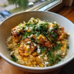 A close-up of a street corn chicken rice bowl featuring seasoned chicken, corn, cotija cheese, and fresh cilantro.