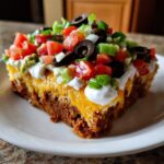 A thick slice of the stunning 7 layer dip showing layers of meat, cheese, sour cream, and fresh toppings like olives and tomatoes.