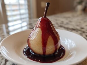 A single, perfectly poached pear drizzled with deep red syrup, served on a white plate.