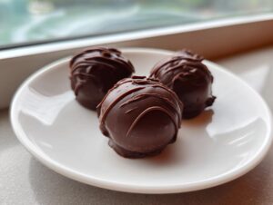 Three decadent chocolate covered Oreo balls drizzled with chocolate, sitting on a small white plate.