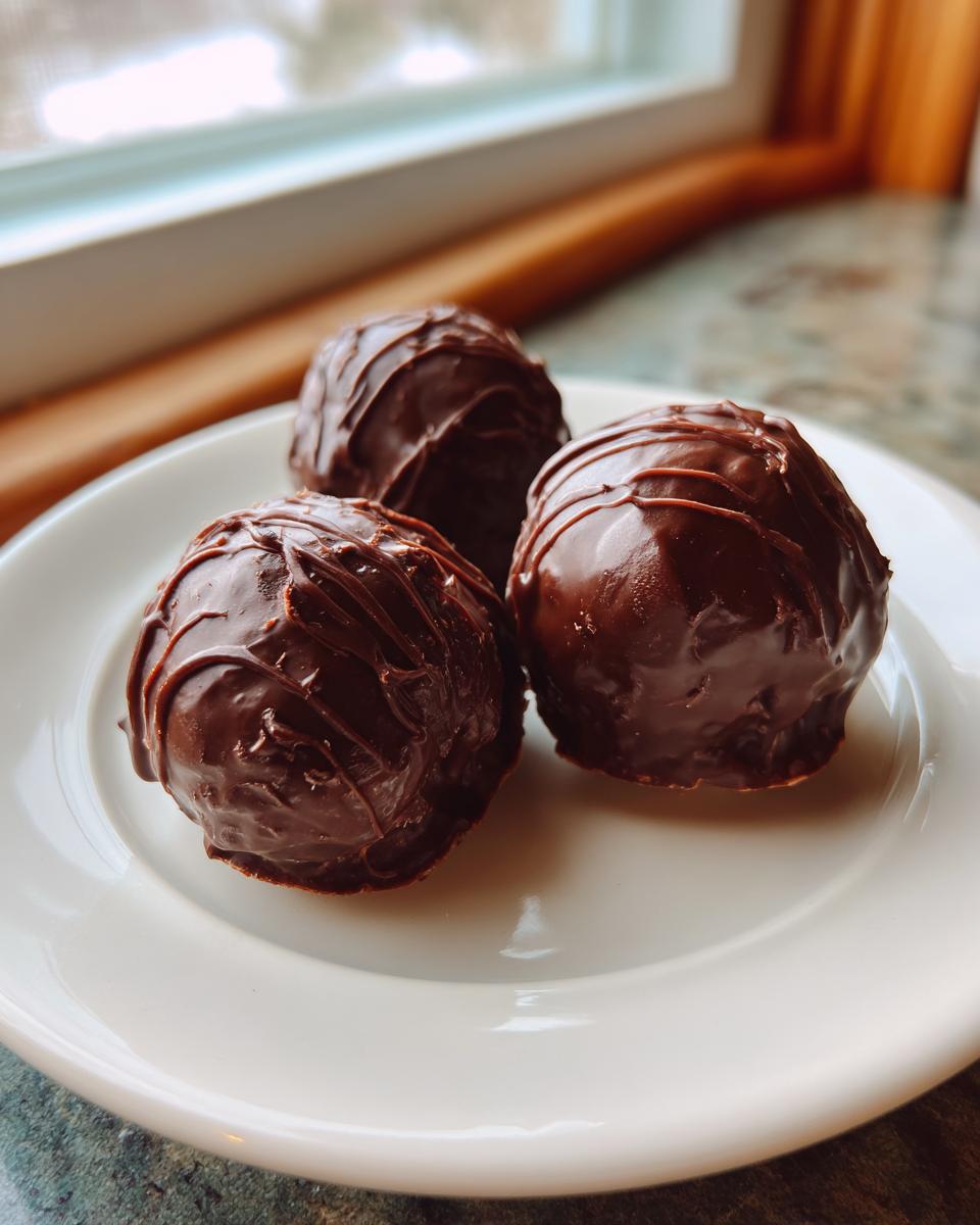 Three decadent, chocolate-covered Oreo balls with drizzled chocolate topping resting on a white plate.
