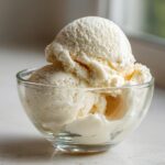 Two scoops of creamy, light-colored protein ice cream served in a small clear glass bowl.