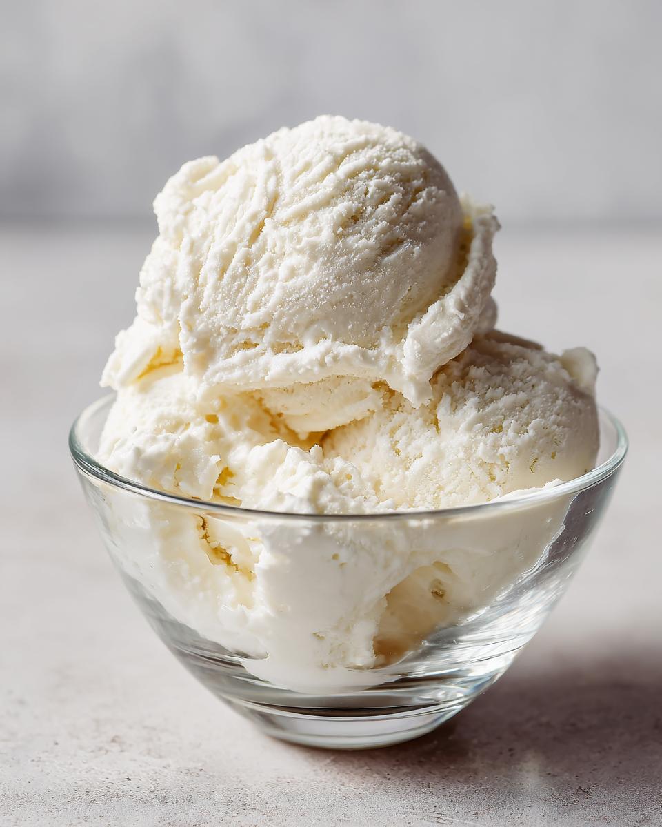 Three scoops of creamy white protein ice cream served in a small clear glass bowl.