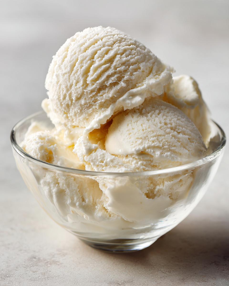 Close-up of several scoops of creamy white protein ice cream served in a clear glass bowl.